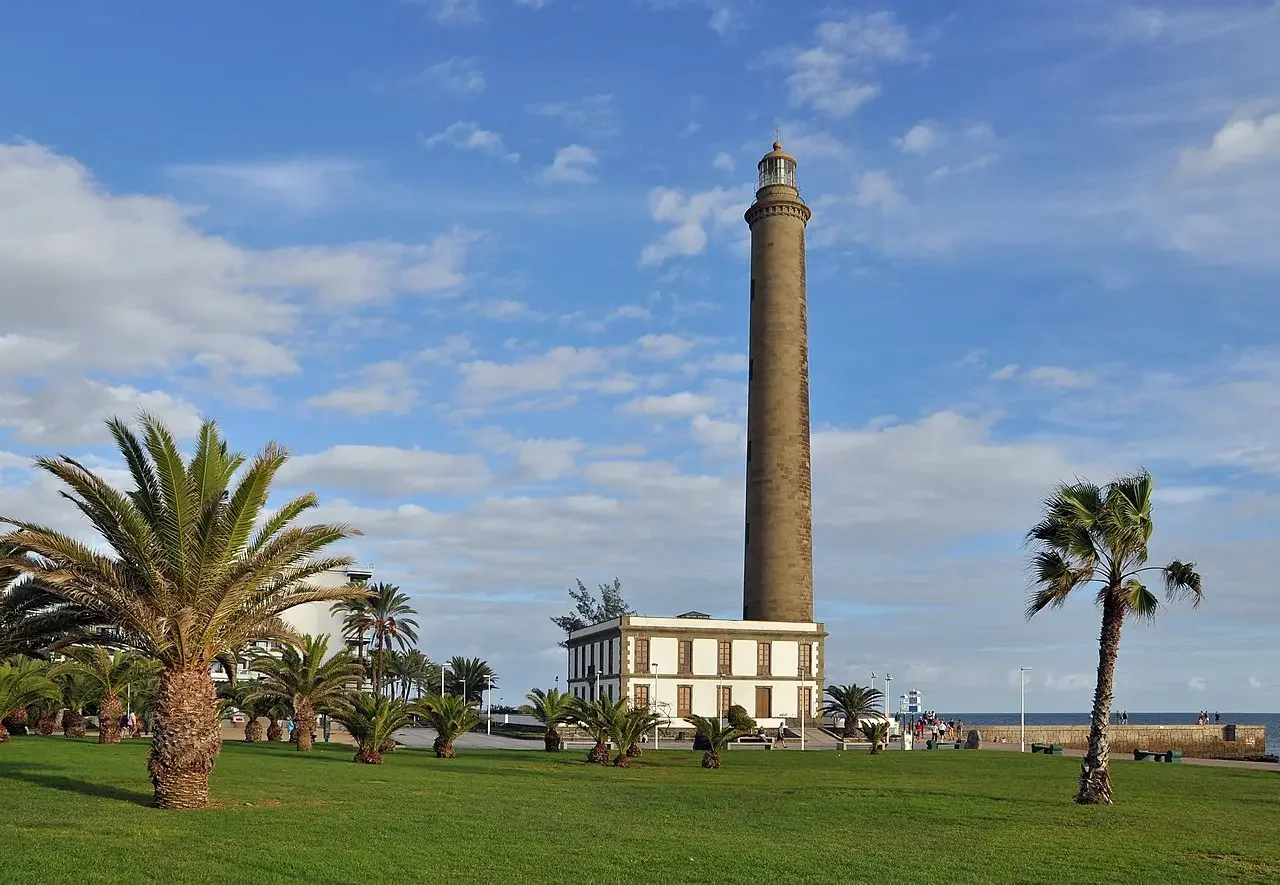 Gente paseando cerca del Faro de Maspalomas en Gran Canaria, con la playa familiar de fondo.