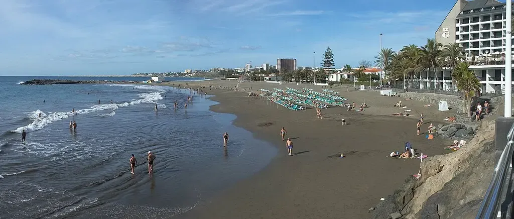 Vista tranquila de la Playa de San Agustín con arena oscura y gente relajándose en hamacas
