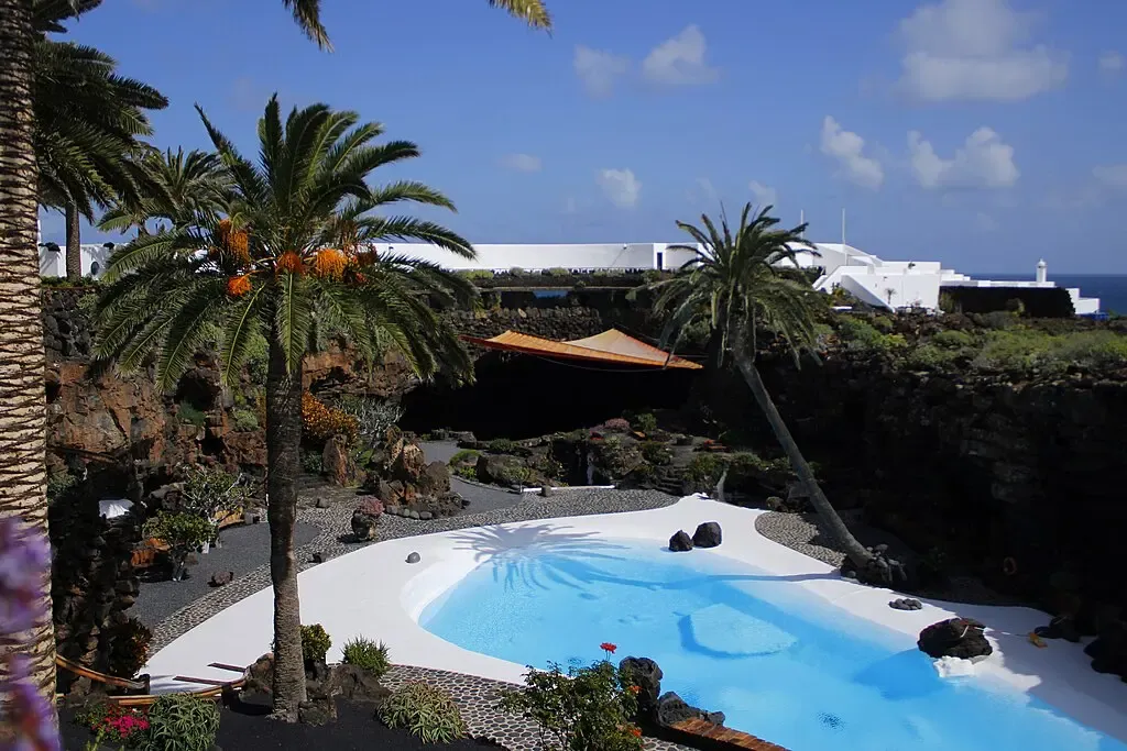 Interior de los Jameos del Agua mostrando el lago subterráneo con reflejos, la piscina blanca de Manrique y la roca volcánica oscura.