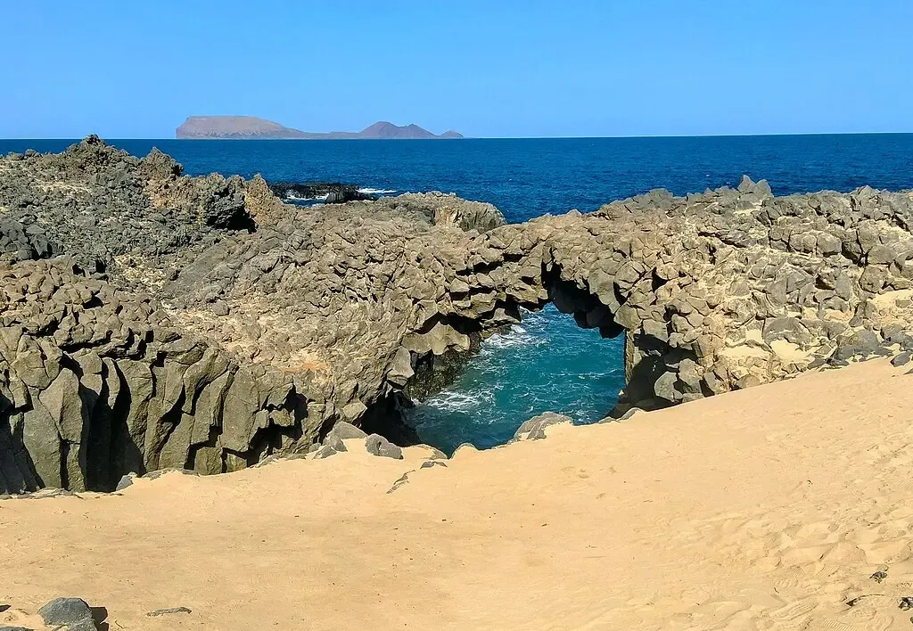 Arco natural de roca volcánica negra (Los Caletones) con el mar rompiendo a través de él