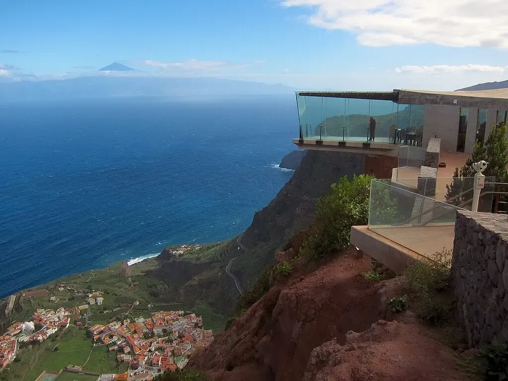 Persona caminando sobre la pasarela de cristal del Mirador de Abrante, con vistas al pueblo de Agulo y al Teide.