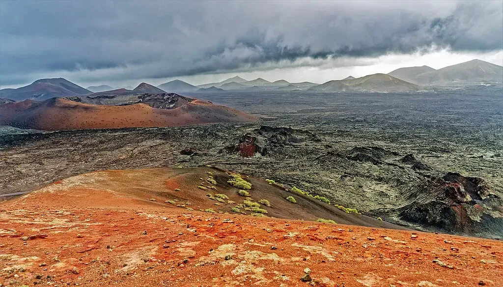 Vista panorámica del Parque Nacional de Timanfaya con las Montañas del Fuego rojas y negras y autobús turístico en la Ruta de los Volcanes.