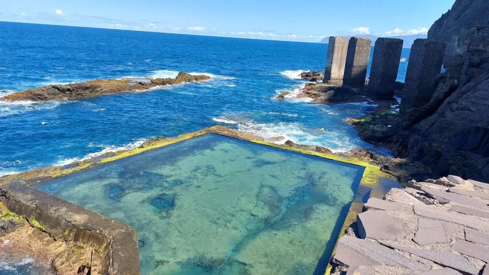 Ruinas de los pilares de hormigón del antiguo Pescante de Agulo adentrándose en el mar bravo.