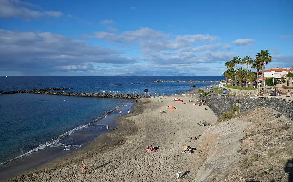 Playa del Duque en Costa Adeje, con arena clara, sombrillas de paja y aguas tranquilas.