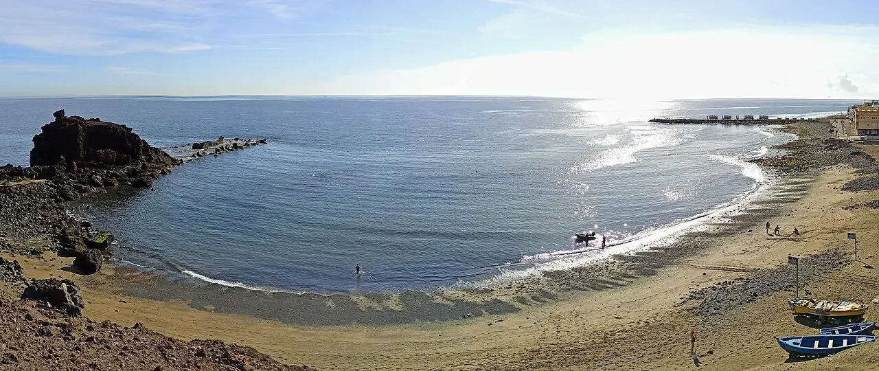 Vista de la playa de El Burrero en Gran Canaria en un día de viento, con la mezcla de arena dorada y negra en primer plano.