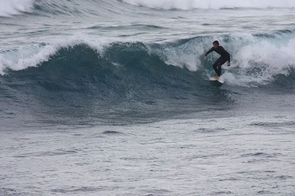 Surfistas aprovechando las olas en la Playa de Famara, Lanzarote, con el imponente Risco de Famara dominando el fondo.