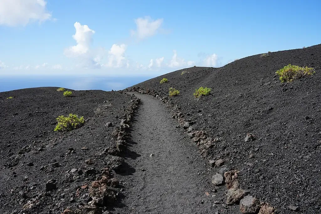 Senderista caminando sobre picón negro en la Ruta de los Volcanes, La Palma.