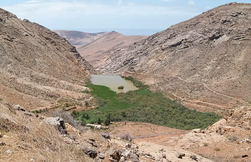 Senderistas caminando por el Barranco de las Peñitas con su palmeral y ermita blanca