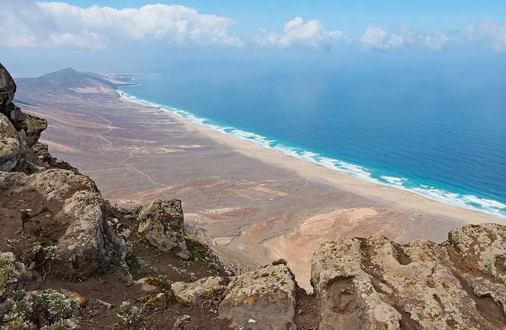 Senderista ascendiendo por el camino hacia el Pico de la Zarza, con vegetación baja y vistas al mar