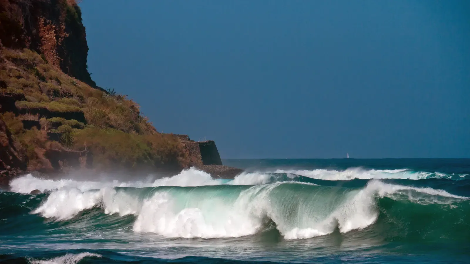 Un surfista cogiendo una ola en la Playa de Santa Catalina, Hermigua, con la costa rocosa de fondo.
